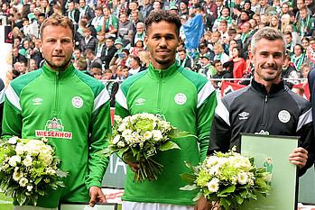 Philipp Bargfrede, Theodor Gebre Selassie und Fin Bartels haben Blumen und Rahmen in der Hand.