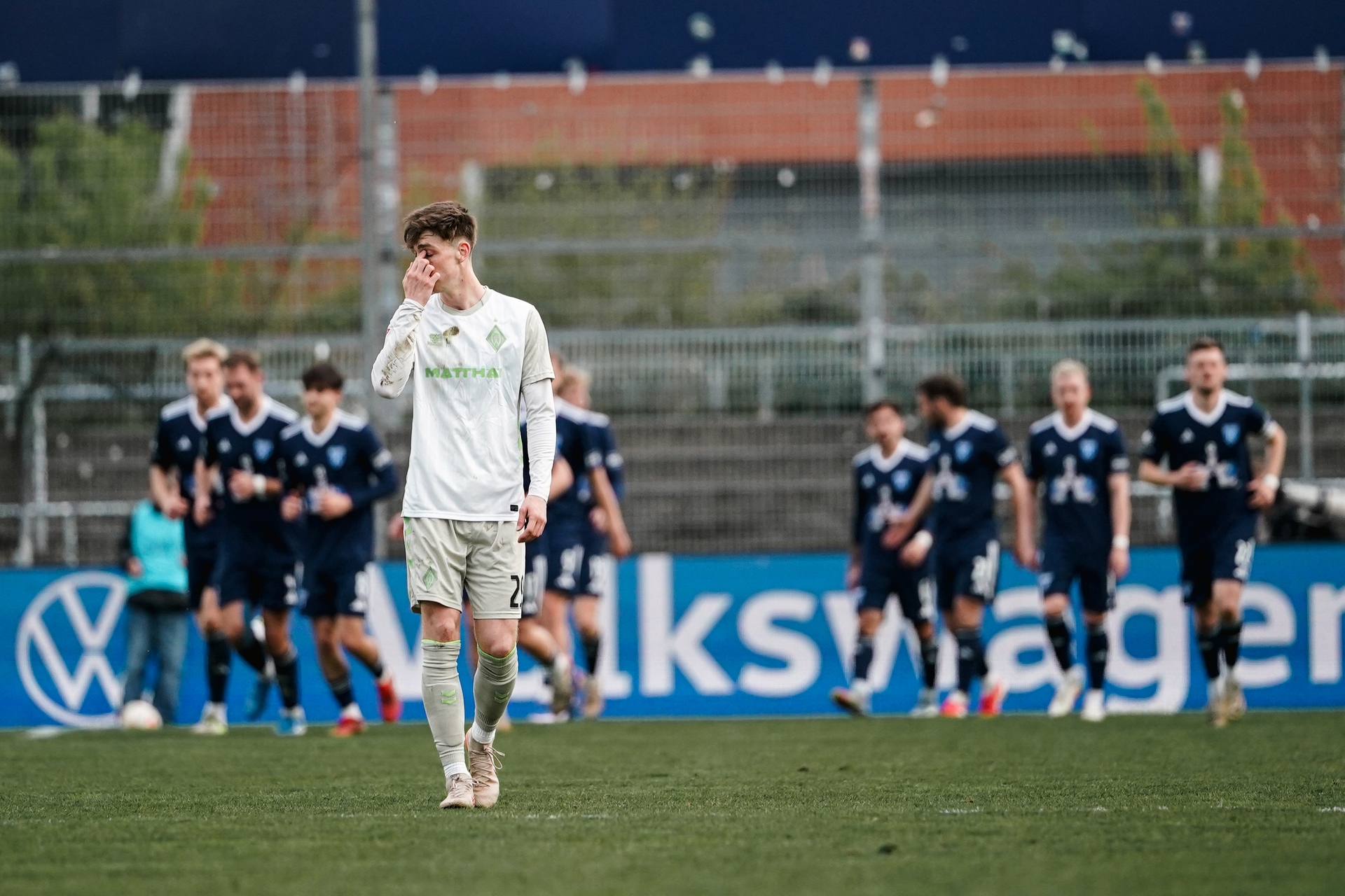 Levi Wagner steht auf dem Rasen, hinter ihm jubeln Spieler von Kickers Emden.