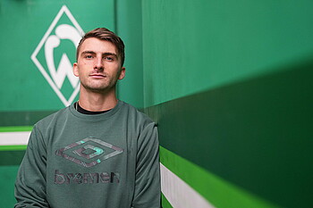Maximilian Philipp vor einer grünen Wand, im Hintergrund ist eine Werder-Raute. 
