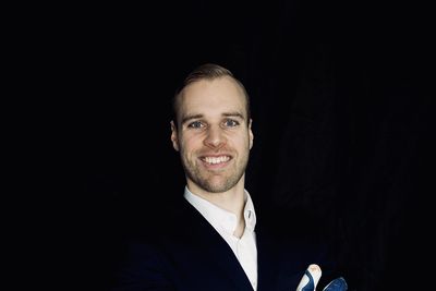 Tom Pachulski mit Torwarthandschuhen in einem Anzug vor einem schwarzen Hintergrund.