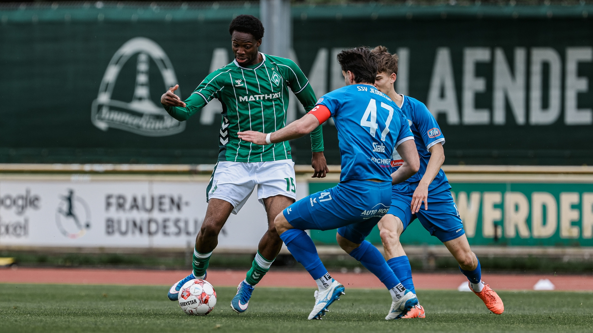 Joel Imasuen führt den Ball am Fuß, während ihm zwei Gegenspieler gegenüberstehen.