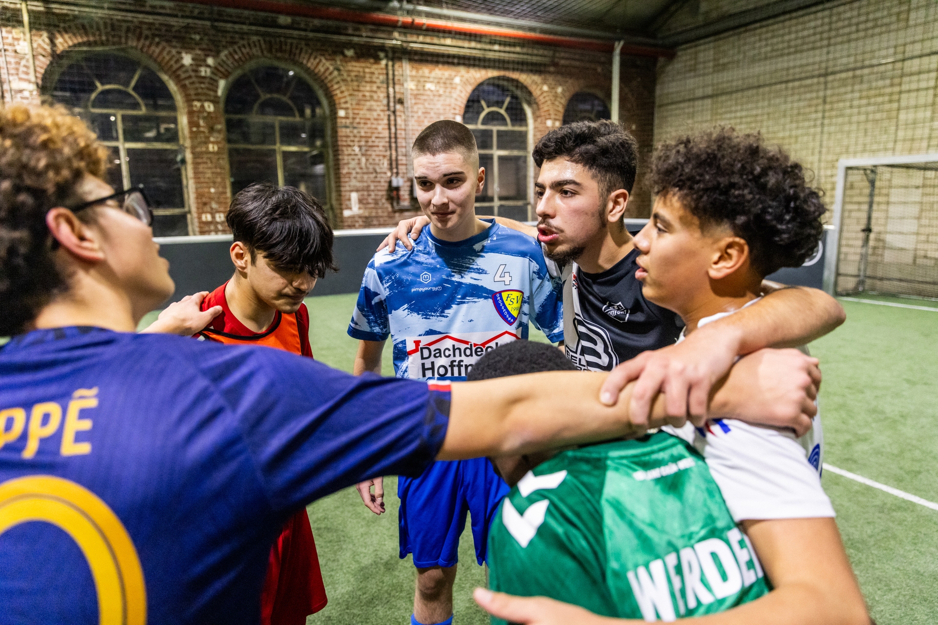 Eine Gruppe junger Fußballspieler in Trikots drängt sich auf einem Hallenfeld zusammen und zeigt Teamgeist und Zusammenhalt.