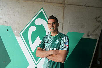 null Rafael Borré trägt das Heimtrikot und steht mit verschränkten Armen vor einer gemalten Werder-Raute.