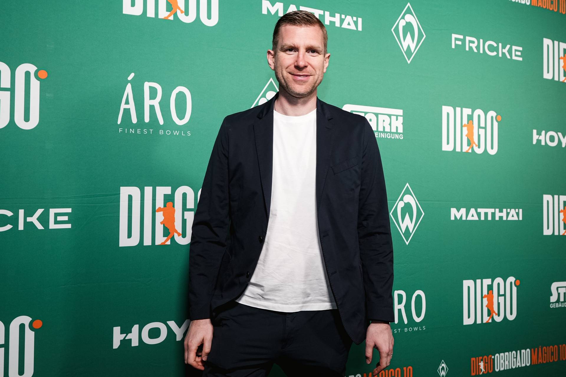 Per Mertesacker im Anzug vor einer Werbewand.