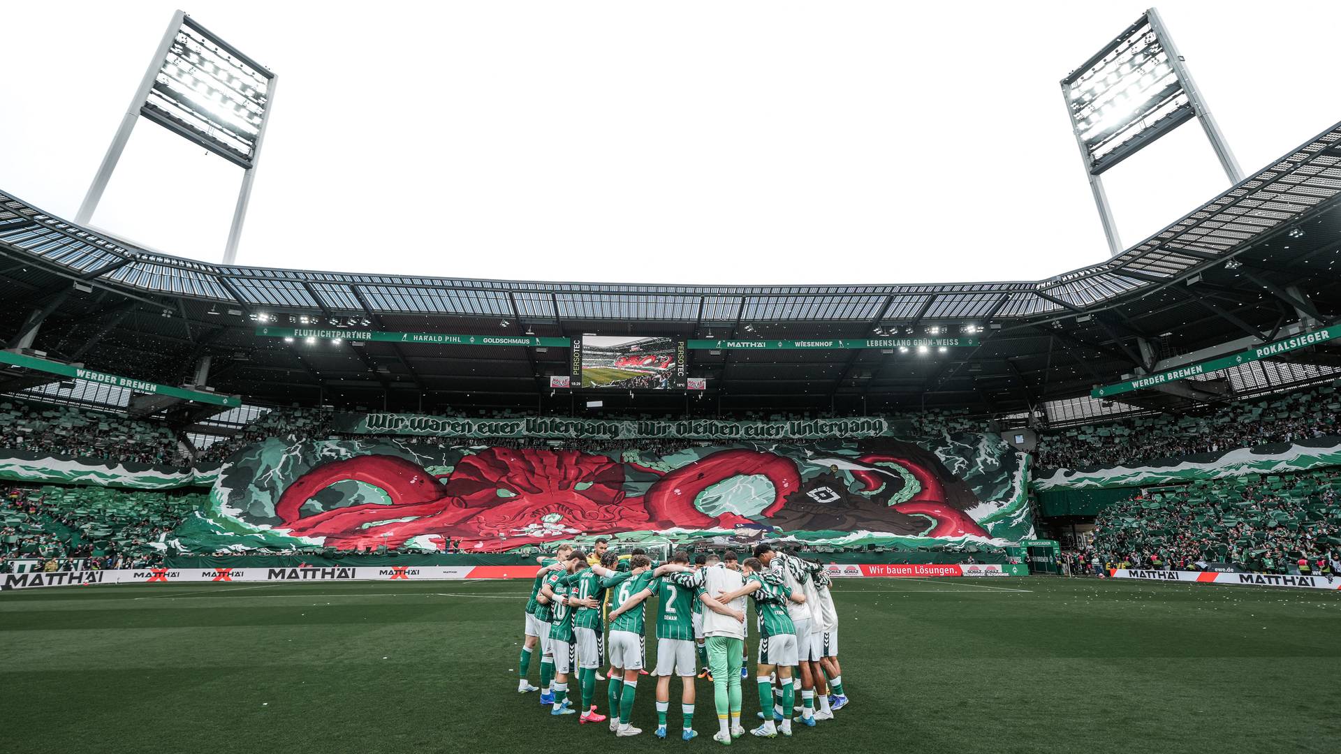 The Werder team are gathered on the pitch, while all around the sold-out stadium hangs a tifo of a red kraken.