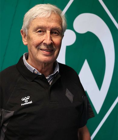 Portrait von Christian Schwarting. Er steht vor einer grünen Wand, auf der die Werder-Raute zu sehen ist.