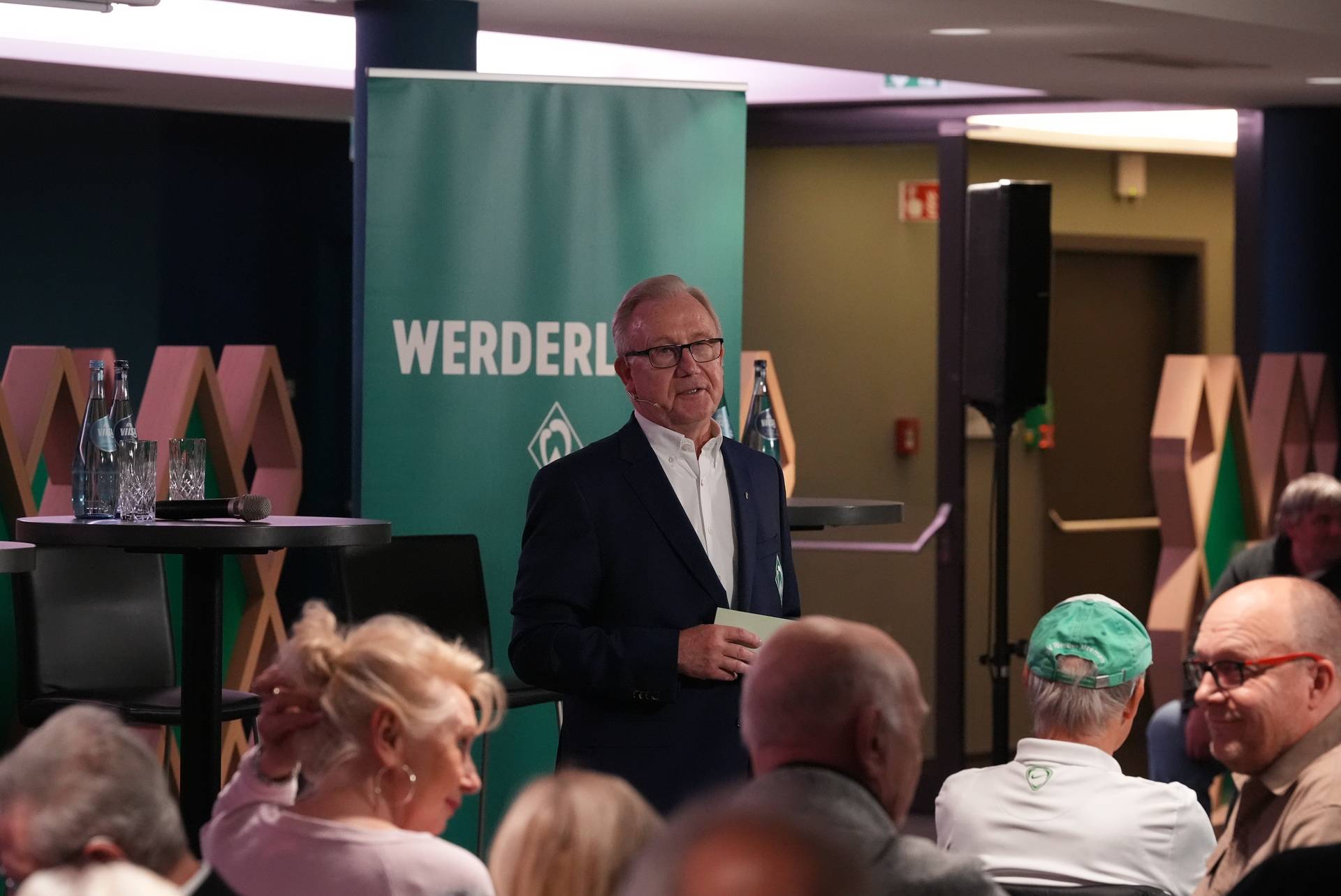 Manfred Jacobi im Anzug vor einem grünen Aufsteller beim Werder-Konvent.