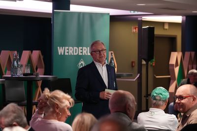 Manfred Jacobi vor einem grünen Aufsteller in einem Anzug beim Werder-Konvent.