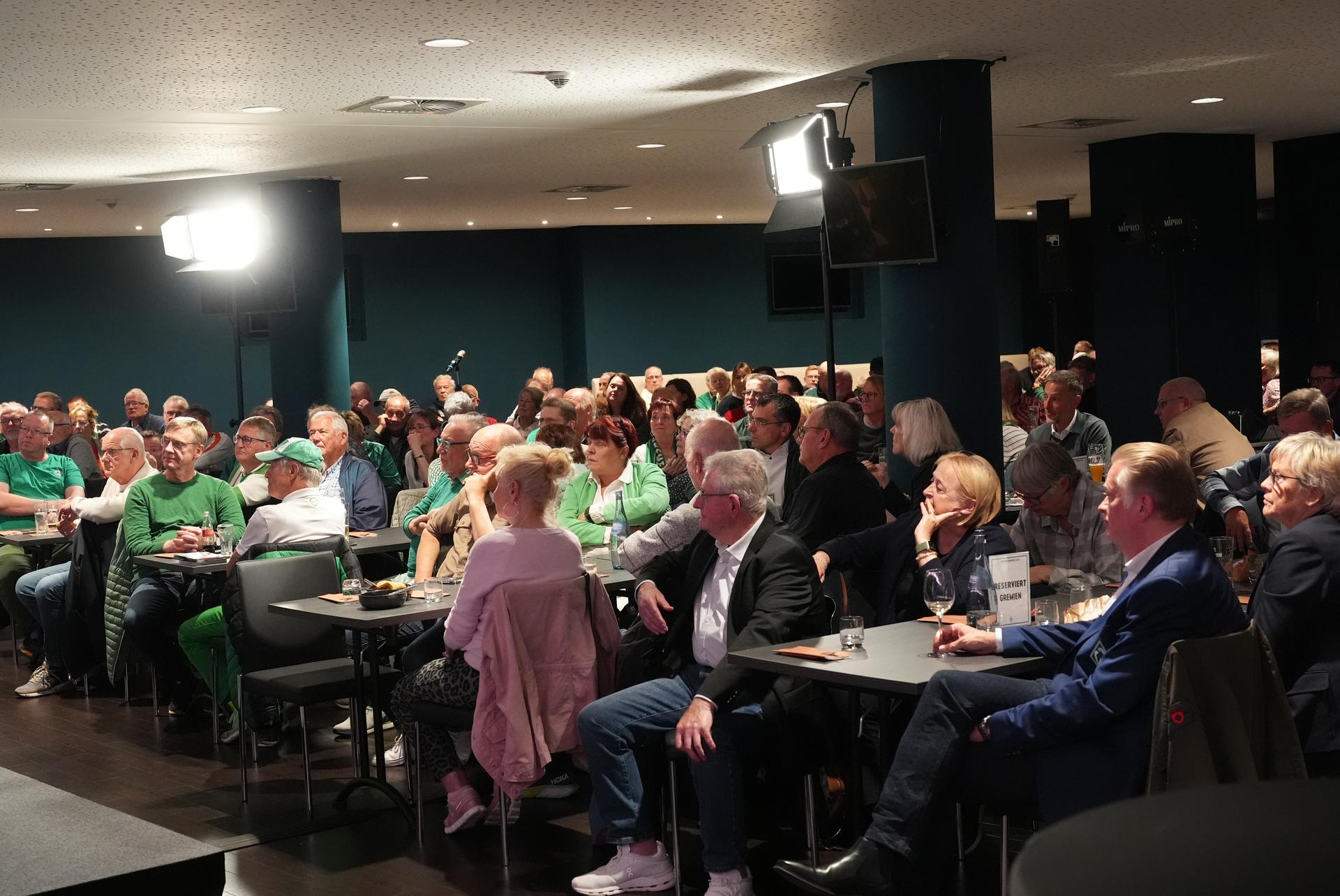 Mitglieder sitzen im Veranstaltungsraum und richten den Blick zur Bühne.