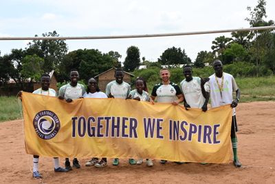 Eine Gruppe von Menschen in Sportbekleidung hält ein Banner mit der Aufschrift „Together We Inspire“ auf einem Feld mit Bäumen im Hintergrund hoch.