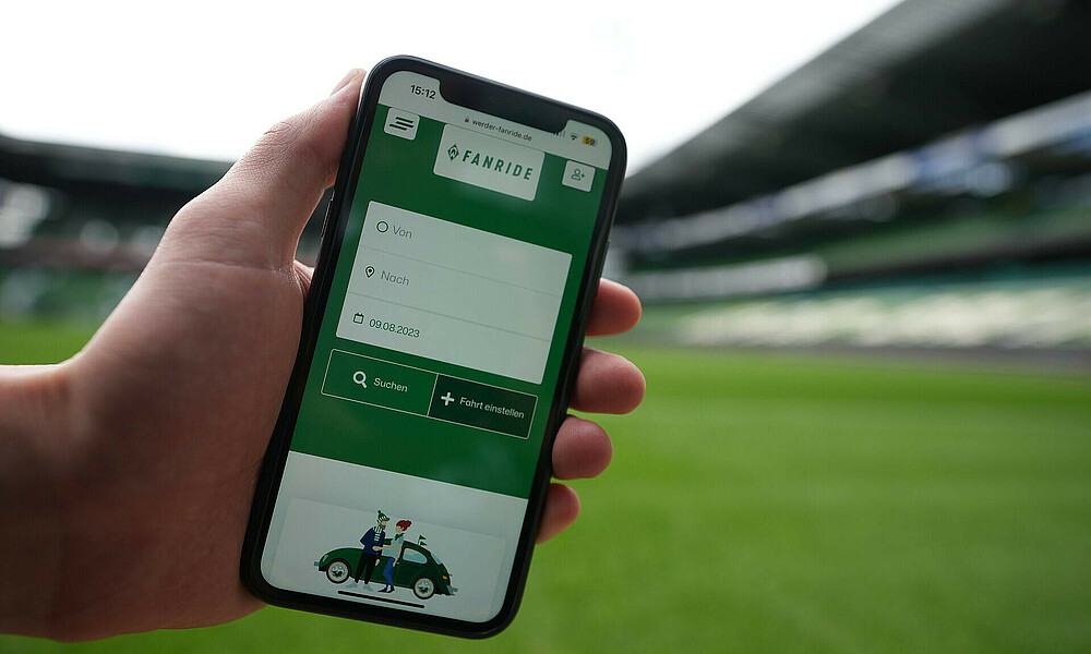 Ein Handy zeigt die Website FanRide - im Hintergrund ist das wohninvest WESERSTADION