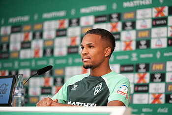 Felix Agu sitzt auf dem Podium im Pressekonferenzraum.