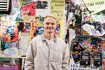 Amos Pieper steht vor einer bunten Wand im Viertel. Die Wand ist beklebt und besprüht.
