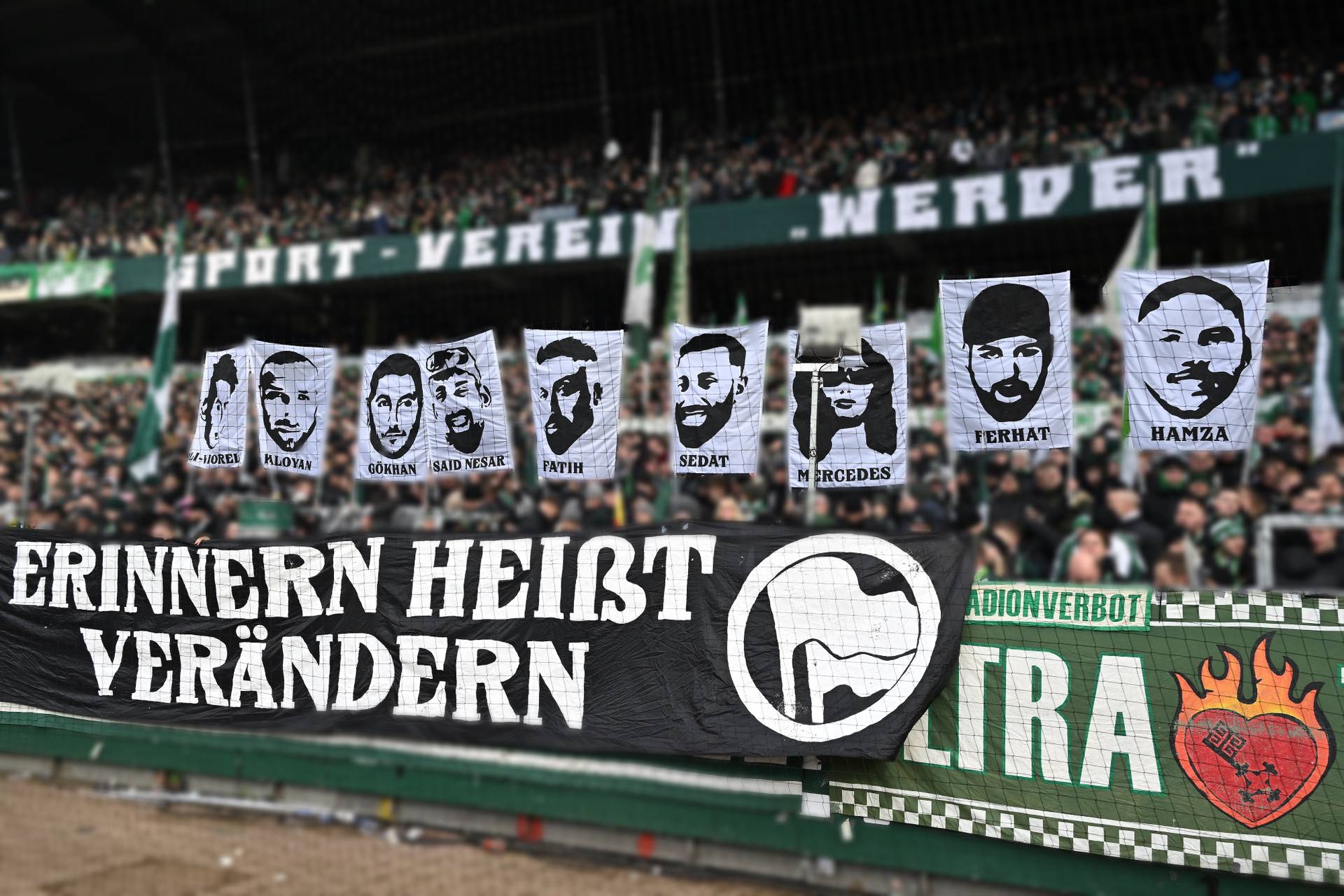 Banner mit Gesichtern und dem Text „Erinnern heißt verändern“, gehalten von Fans in einem überfüllten Sportstadion, mit dem Namen der Mannschaft „Werder“ sichtbar.