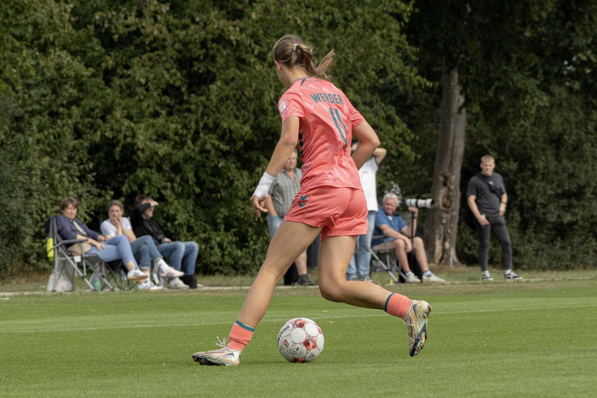 Eine Spielerin der 2. Frauen im korallfarbenen Dress dribbelt mit dem Ball.