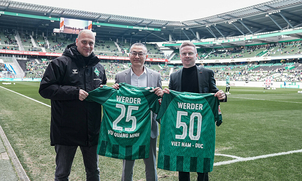 Klaus Filbry, Vu Quang Minh und Dominik Kupilas halten ein Trikot. 