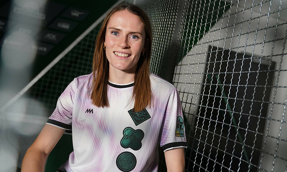 Reena Wichmann sitzt vor einem Gitter im Common Goal-Trikot