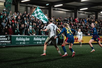 Larissa Mühlhaus im Zweikampf mit einer Spielerin von Leipzig, im Hintergrund sieht man die Werder-Fans im Gäste-Block.