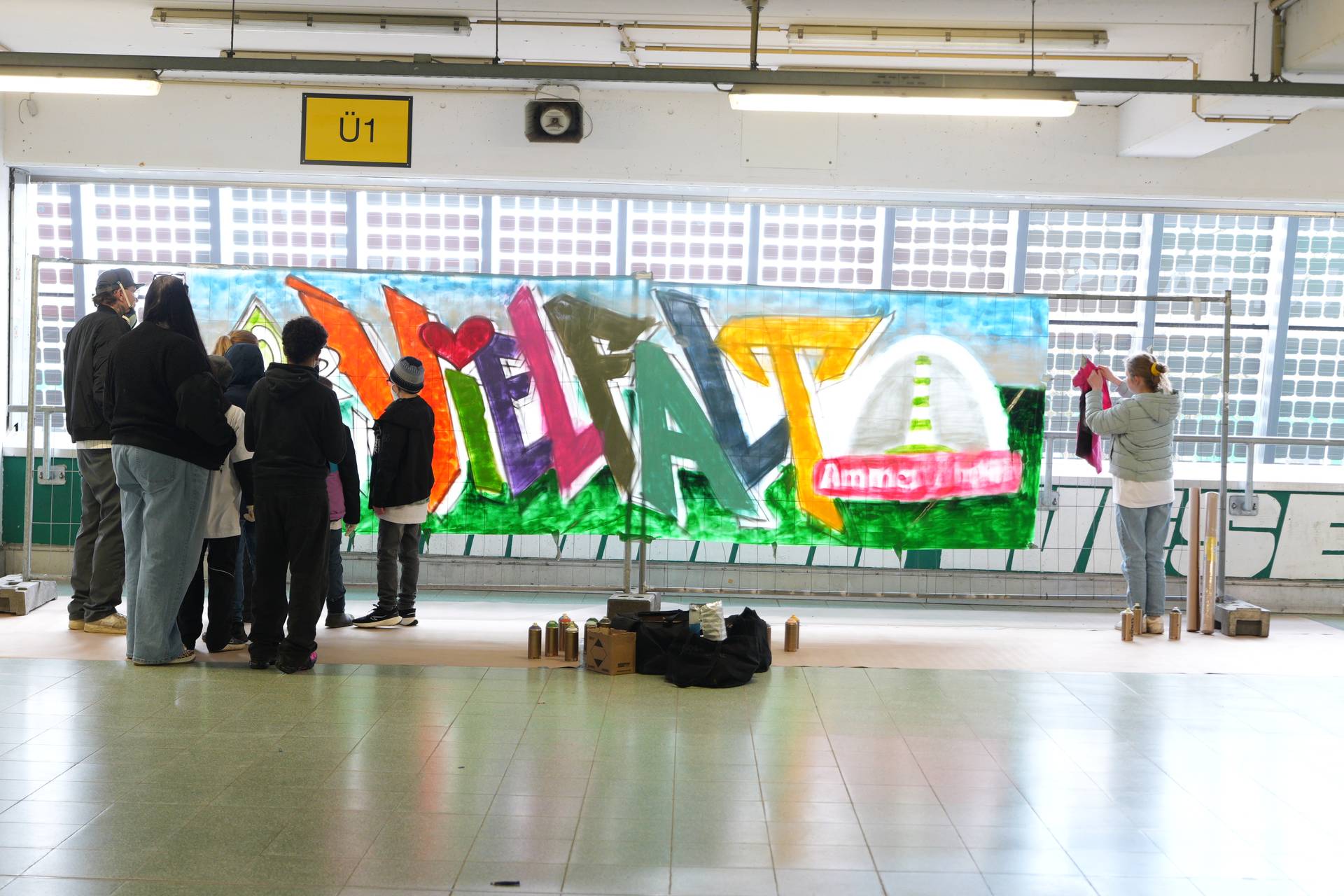 Menschen betrachten in einem Innenraum ein farbenfrohes Graffiti-Wandbild auf einer großen Leinwand, das sich durch lebhafte Buchstaben und Formen auszeichnet.