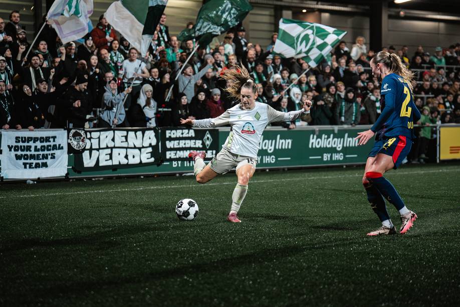 Michelle Weiß setzt zum Schuss an. Im Hintergrund sind Werder-Fans zu sehen, ie Fahnen schwenken und anfeuern.