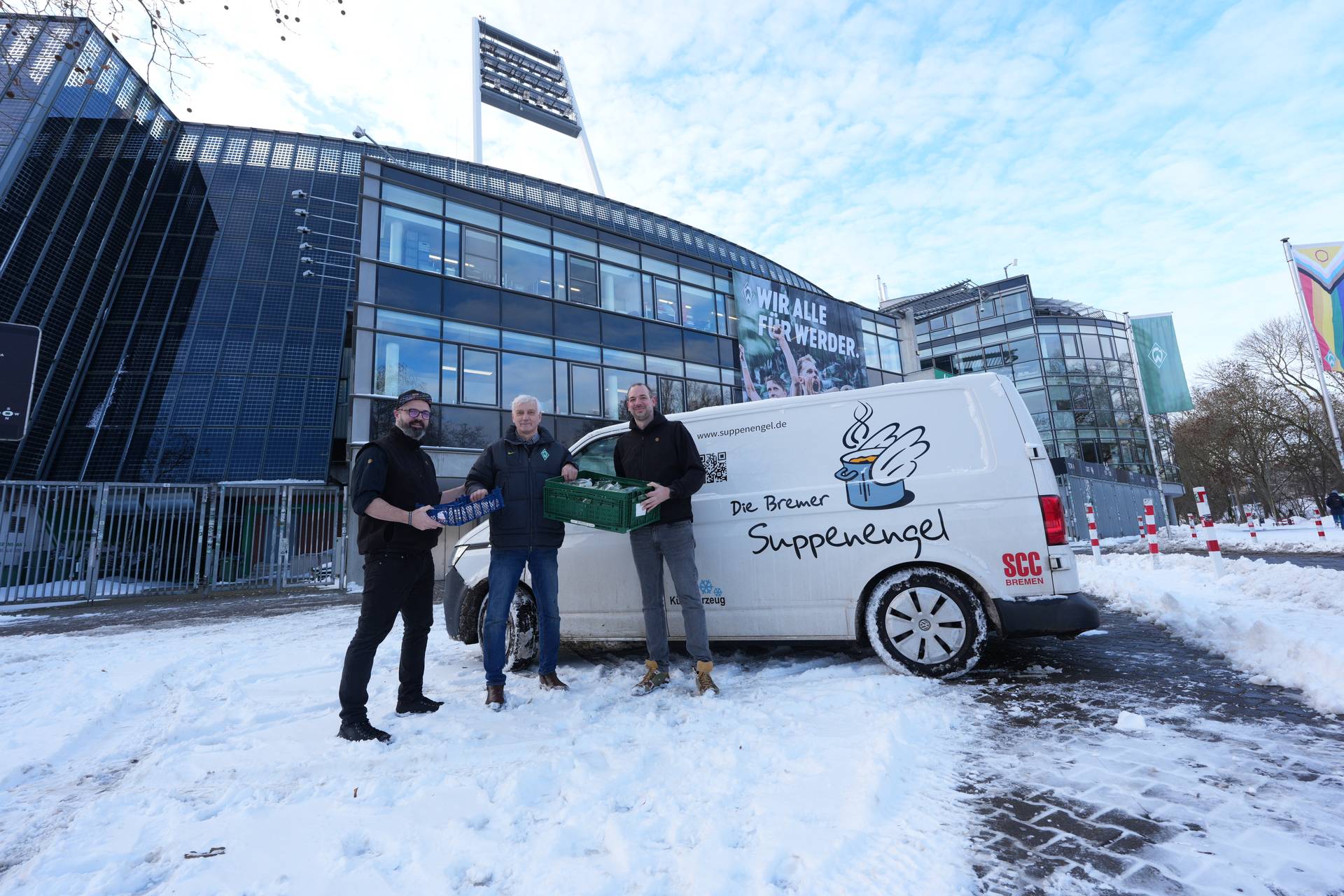 Drei Männer stehen vor einem weißen Lieferwagen mit der Aufschrift „Die Bremer Suppenengel“ in der Nähe eines Gebäudes, umgeben von Schnee.
