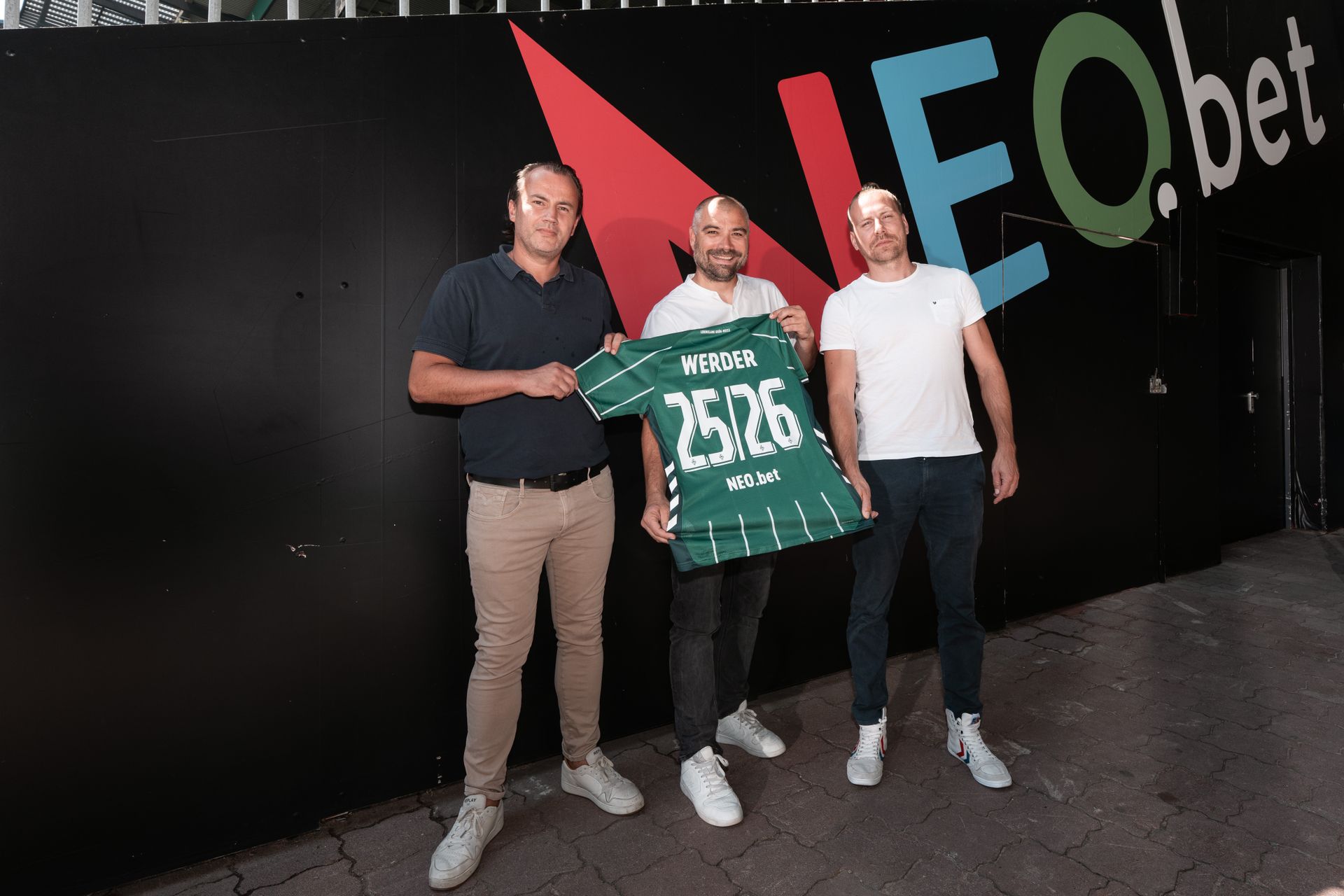 Mehrere Personen stehen vor einer Wand mit neobet-Aufdruck. Sie halten ein Werder-Trikot in der Hand.