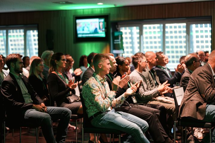 Eine sitzende Menschenmenge in einem Saal applaudiert.