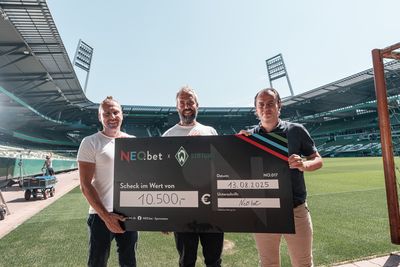 Drei Männer stehen auf einem Fußballfeld und halten einen großen Scheck über 10.500 Euro in den Händen. Im Hintergrund ist das Stadion zu sehen.
