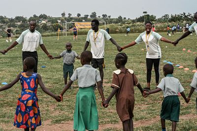 Kinder und Erwachsene stehen Hand in Hand im Kreis auf einer Wiese und nehmen an einer Gruppenaktivität oder einem Spiel im Freien teil.