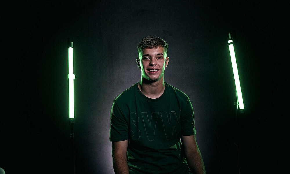 Keke Topp sitzt vor schwarzem Hintergrund. Rechts und links von ihm leuten grüne Stäbe.