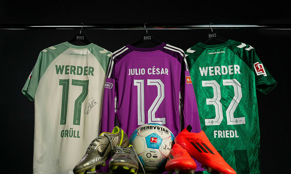 Auf dem Bild sind getragene und signierte Werder-Trikots sowie Fußballschuhe und ein Ball.