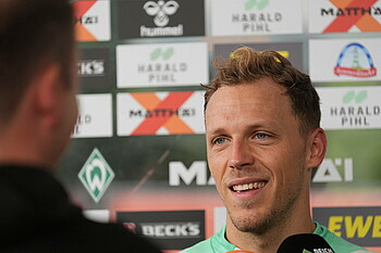 Senne Lynen wird interviewd. Man sieht ihn und Kameras vor einer Sponsorentafel.