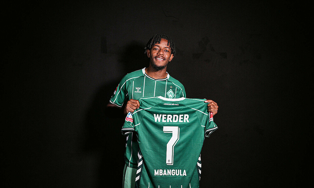 Samuel Mbangula mit einem Werder-Trikot in der Hand.