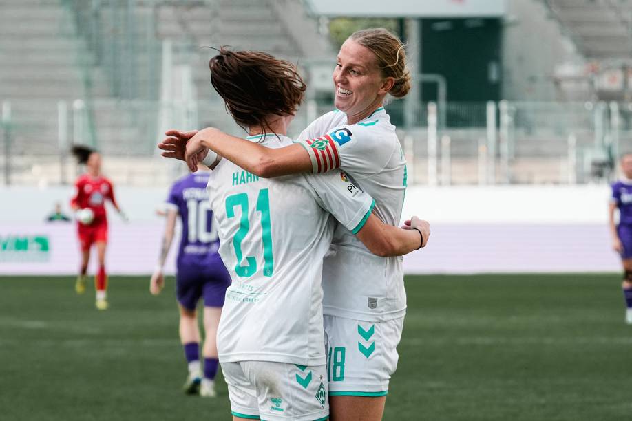 Lina Hausicke im weißen Trikot und weißer Hose lacht. Sie umarmt eine andere Spielerin.