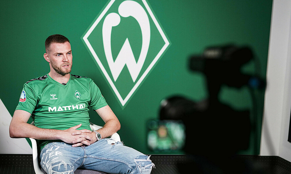Marvin Ducksch vor der Kamera, im Hintergrund eine Werder-Raute. 