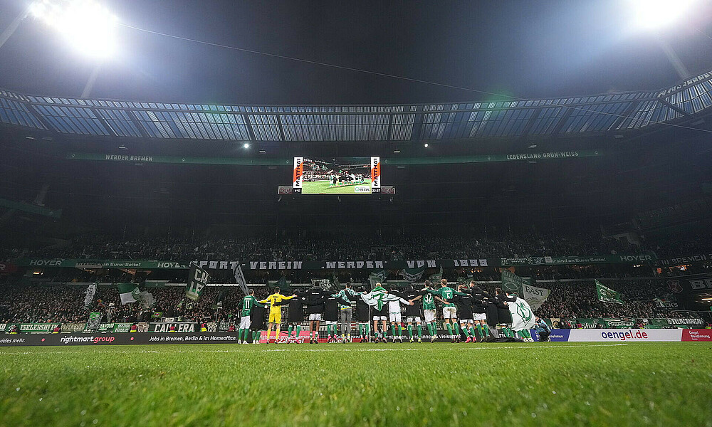 Die Mannschaft feiert vor der Ostkurve im Flutlichtbeleuchteten Weserstadion, Ansicht von hinten