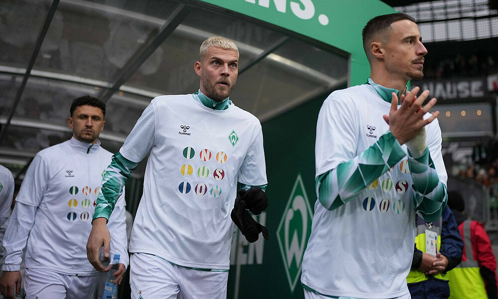 Marco Friedl und Marvin Ducksch laufen zum Warm Up ein. Sie tragen ein Shirt mit dem Schriftzug Inklusion