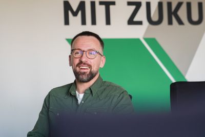 Edgar Kary sitzt vor einer grün-weißen Wand und spricht in die Kamera.