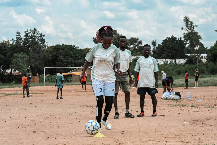 Eine junge Fußballspielerin in einem Trikot von Werder Bremen übt auf einem Feld aus Erde das Dribbeln, umgeben von ihren Mannschaftskameraden und Bäumen im Hintergrund (FOTO: W.DE).