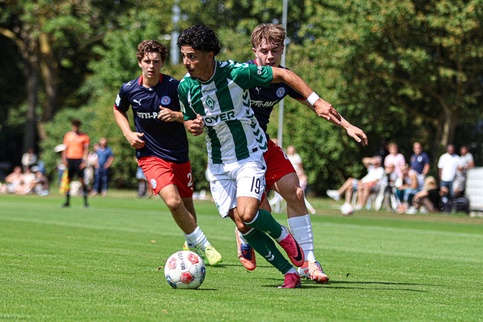 Ein Spieler der U19 läuft mit dem Ball am Fuß und wird von seinen Gegenspielern verfolgt.