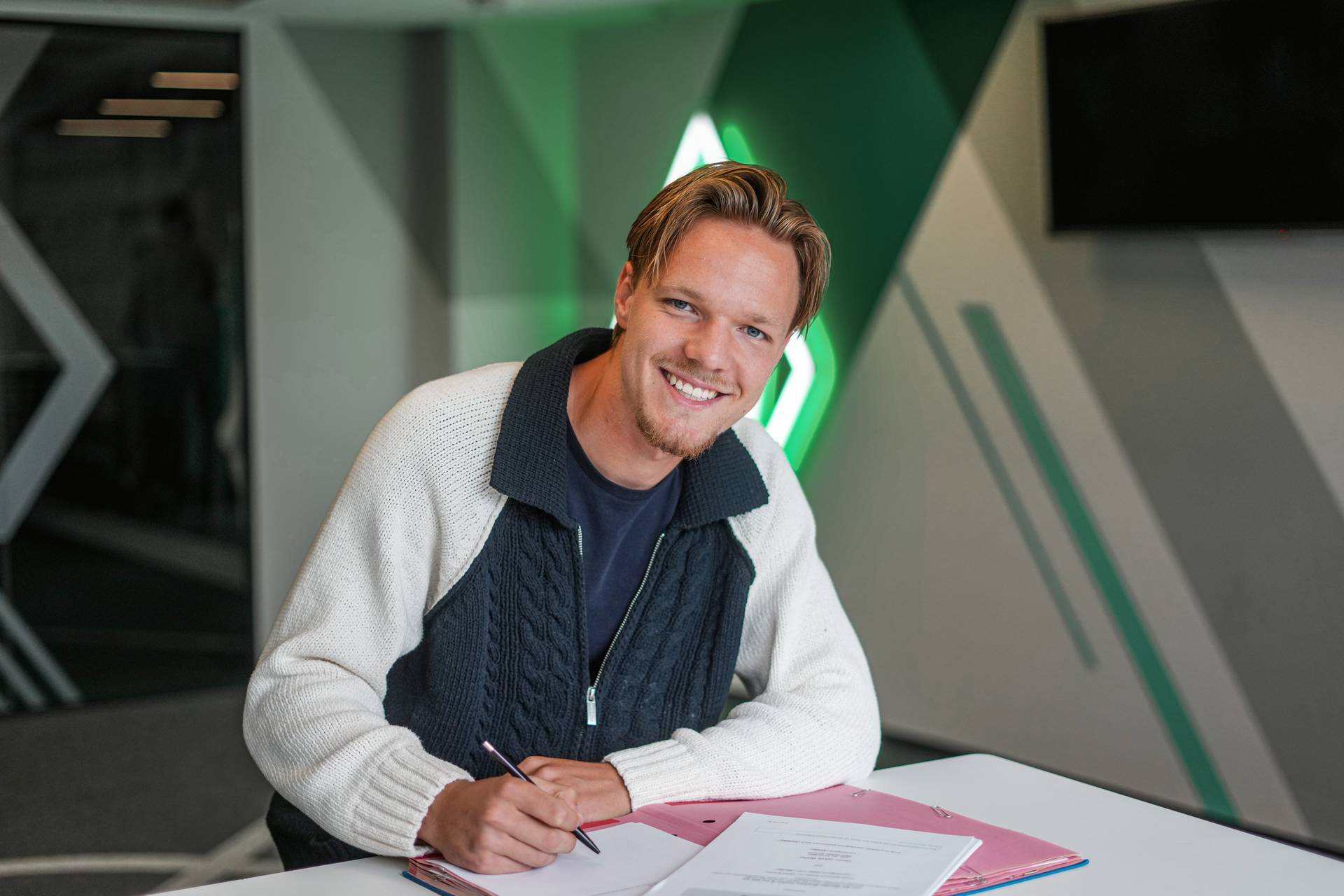 Jakob Wiehe sitzt an einem Tisch und unterschreibt einen Vertrag.