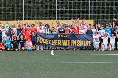 Alle Teilnehmenden der Vereine stehen auf einem Fußballfeld und halten ein Banner in die Höhe worauf "Together we inspire" steht