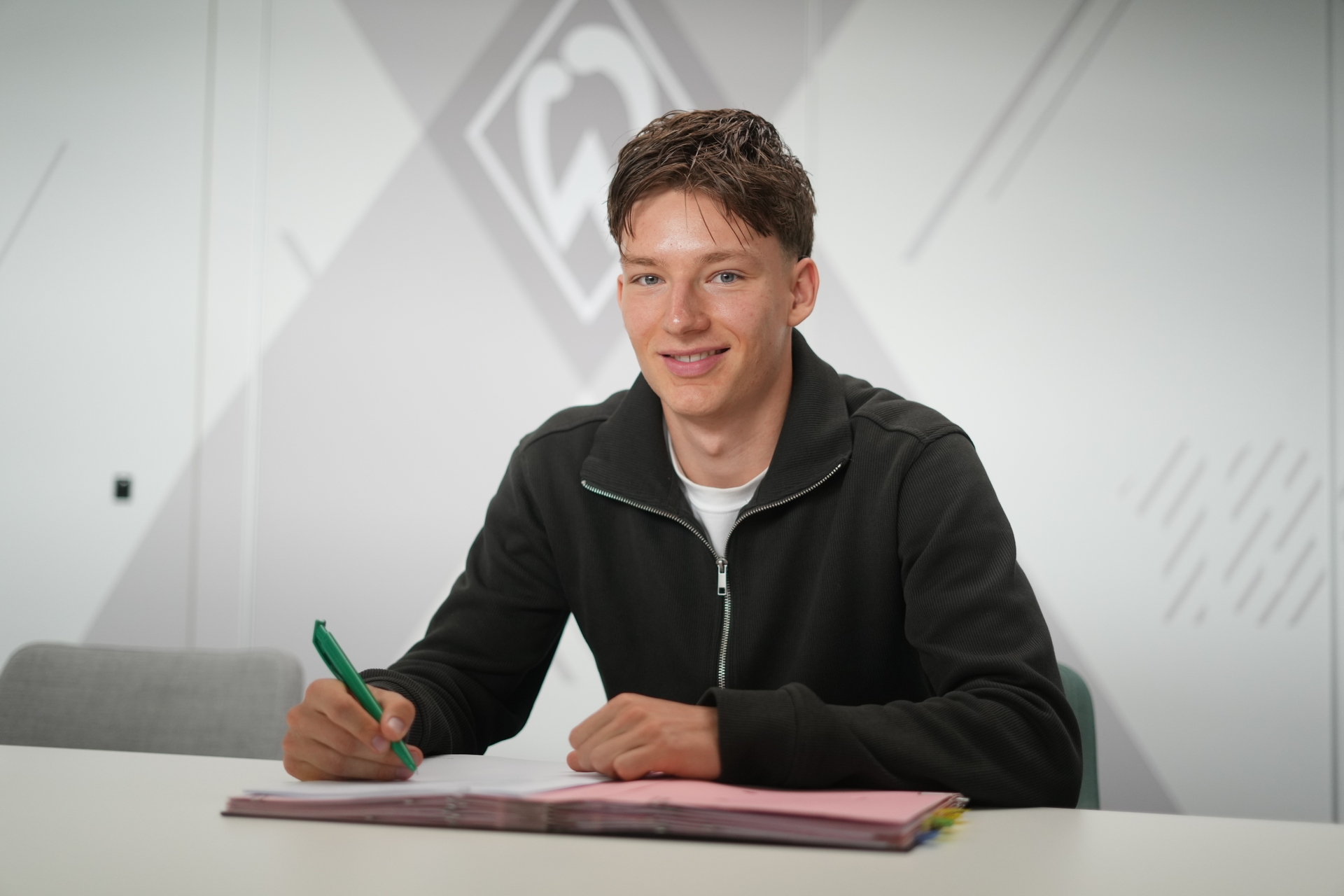 Karlo Simic sitzt mit einem Stift in der Hand und einem Vertrag vor sich liegend an einem Tisch.