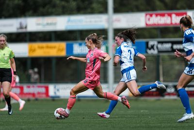 Michelle Weiß in einer rosa Spielkleidung dribbelt den Ball, während eine Spielerin in Blau und Weiß auf einem Rasenfeld versucht, sie einzuholen.