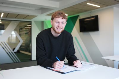 Johann Wegner sitzt an einem Tisch. Vor ihm liegt ein Vertrag. Er hat einen Stift in der Hand.