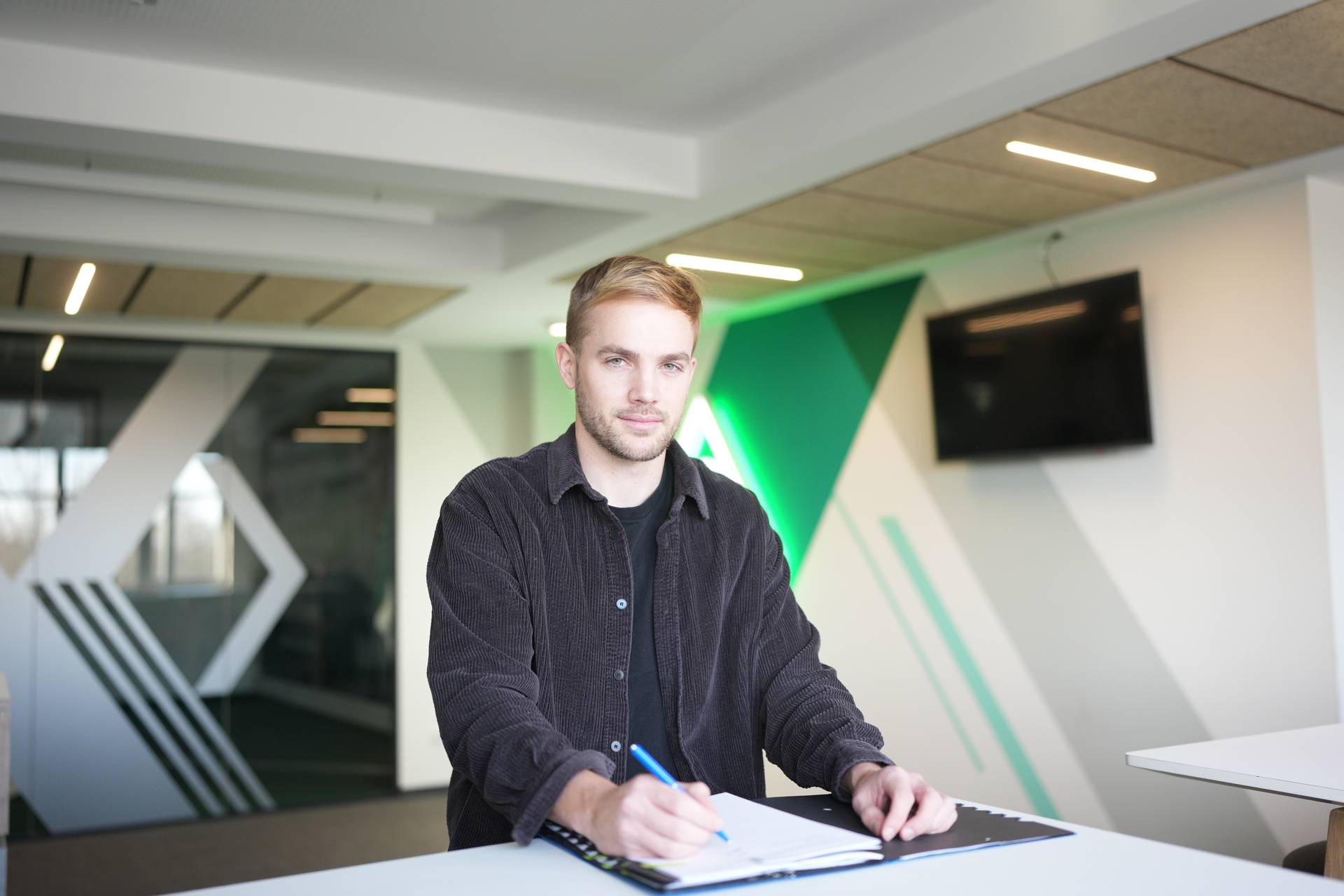 Cimo Röcker sitzt vor der Werder-Raute und unterschreibt seinen Vertrag.