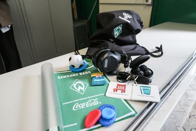 Inhalt des Sensoriktäschchens: Kopfhörer, Stressball, Ohrstöpsel, Sonnenbrille, Sensorikkarten, grüne Matte und ein schwarzer Beutel mit Kordelzug auf einem Tisch.