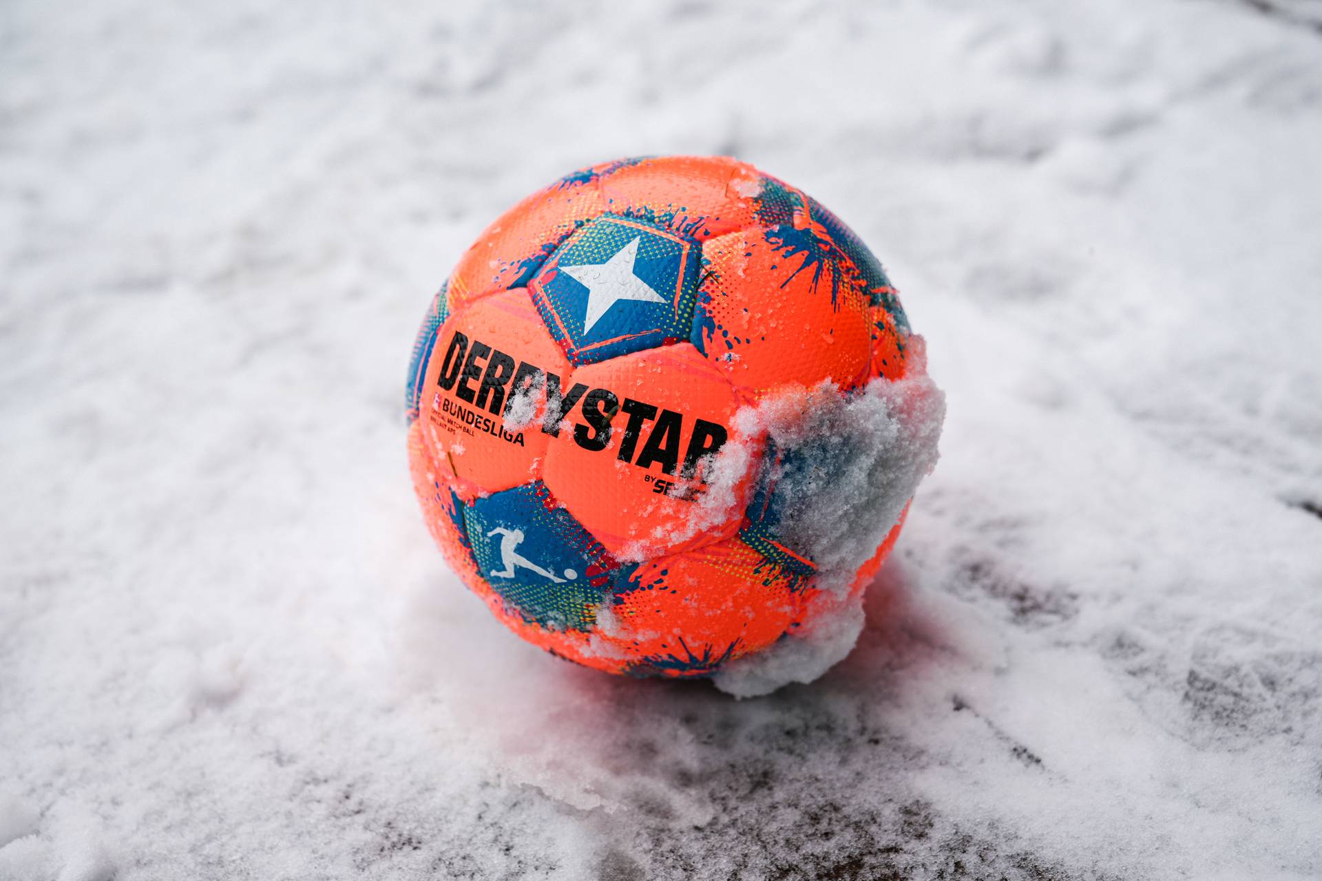 Ein orangener Fußball liegt im Schnee.