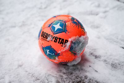 Ein orangener Fußball liegt im Schnee.