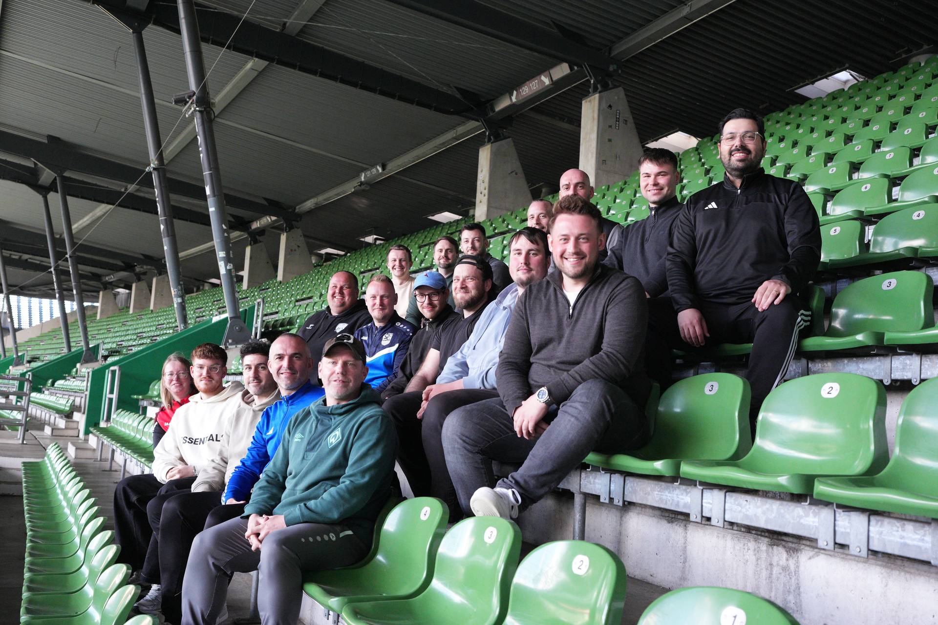 Eine Gruppe von Menschen sitzt auf grünen Stühlen auf der Tribüne im Weserstadion.